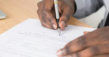 Personne Tenant Un Stylo Torsadé Gris Et Papier D'imprimante Blanc Sur Une Table En Bois Brun